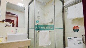 A bathroom with a glass-enclosed shower, a sink, and a toilet. There is a towel hanging on the wall and a sign indicating the hotel name.