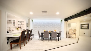 A modern dining area with a white textured wall, a kitchen with white cabinets, and a dining table with chairs.