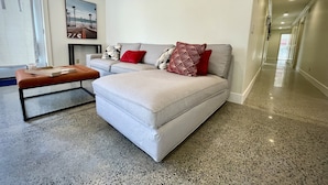 A modern living room with a light-colored sofa, a wooden coffee table, and a red cushion.