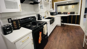 A modern kitchen with white cabinetry, a black stove, and a microwave. There is a wooden floor and a dining area visible in the background.