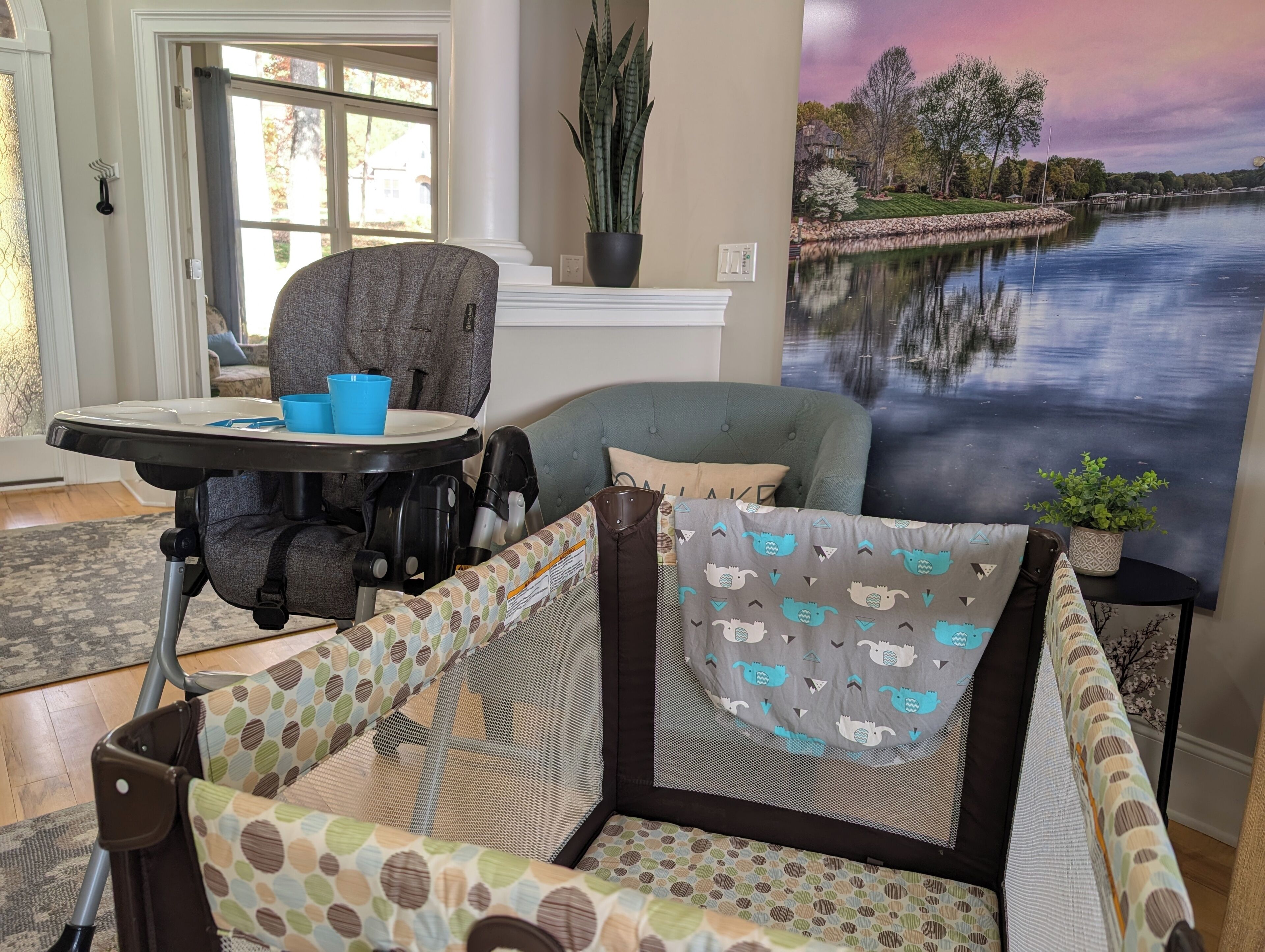 Een kamer met uitzicht op een meer, een eettafel met blauwe bekers, een grijze fauteuil en een gestreept sofa.