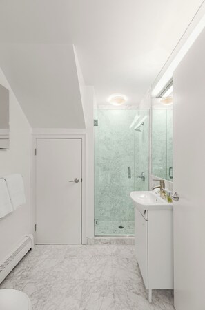 A modern bathroom with a white door, a glass shower enclosure, and a white sink with a mirror.