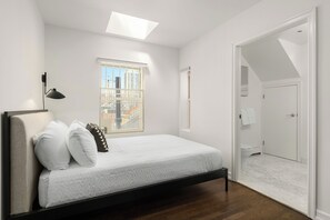 A bedroom with a bed, a skylight, a window, and a view of the city.