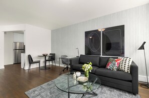 A modern living room with a glass coffee table, black sofa, and a dining area with a glass table and chairs.
