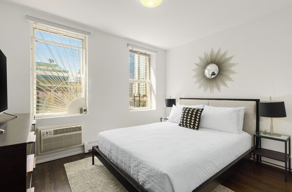 Une chambre moderne avec un grand lit, deux fenêtres, un miroir fixé au mur et un radiateur.