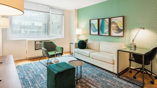 Ein modernes Wohnzimmer mit einer Wand in Grün mit Muster, einem weißen Sofa, einem grünen Sessel, einem kleinen runden Tisch und einem Glastisch mit Stuhl.