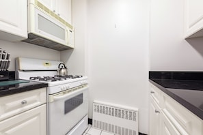A compact kitchen with white cabinetry, a gas stove, a microwave, and a built-in oven.