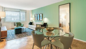 Ein modernes Wohnzimmer mit einem Glastisch, grünen Polsterstühlen, einem weißen Sofa und einer Wand mit grünem Muster.
