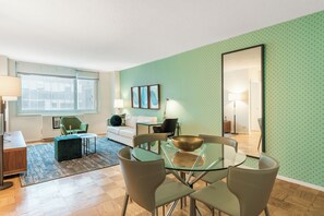 Un soggiorno moderno con un tavolo da pranzo in vetro, sedie rivestite in verde, un divano bianco e una parete decorata con un motivo verde.