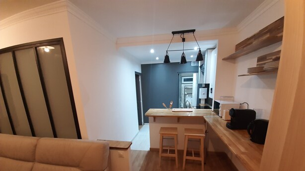 A modern kitchen with wooden countertops, a central island with stools, and a built-in oven. - 2-room apartment, near RER, bus and castle (Rambouillet)