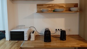 A kitchen with wooden shelves, a microwave, a toaster, and a coffee maker on a wooden countertop. - 2-room apartment, near RER, bus and castle (Rambouillet)