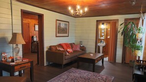 Ein gemütliches Wohnzimmer mit Sofa, Couchtisch und Teppich. Eine Lampe, ein Bilderrahmen und ein kleiner Tisch mit Lampe sind vorhanden. Eine Pflanze hängt von der Decke.