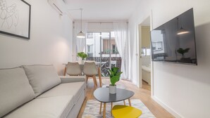 A modern living room with a sofa, a small table with a plant, and a TV mounted on the wall.
