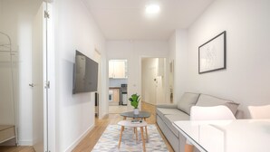 A modern living room with a sofa, a coffee table, and a TV. There is a kitchen area in the background.