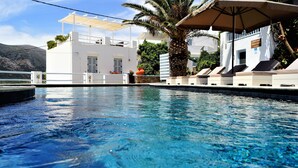 Área de piscina com espreguiçadeiras e um edifício branco com varanda coberta.