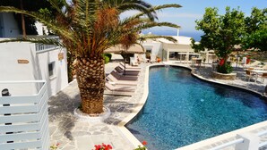 Uma área de piscina com espreguiçadeiras, uma placa de recepção e uma palmeira.