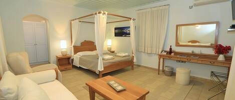 Une chambre à coucher avec un lit à baldaquin, une table de chevet avec une lampe, une commode en bois, un canapé, une table basse, un miroir et un téléviseur fixé au mur.