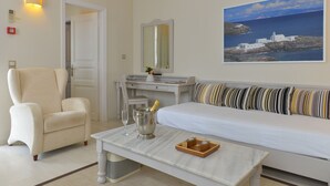 Um quarto com um sofá branco, uma poltrona branca, uma mesinha com uma garrafa de champanhe e um quadro de uma paisagem costeira.