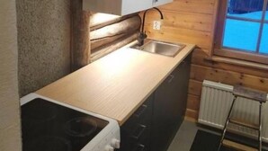 A compact kitchen with a stove, sink, and wooden cabinets. - Kuukkeli Log Houses Aurora- Secret Cabin (Saariselka)