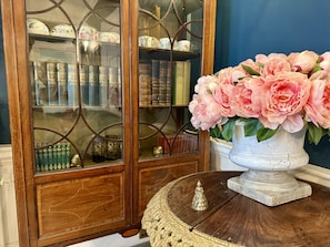 Un meuble en bois avec des portes en verre, un vase blanc orné de fleurs roses et une petite figurine posée sur une table ronde.