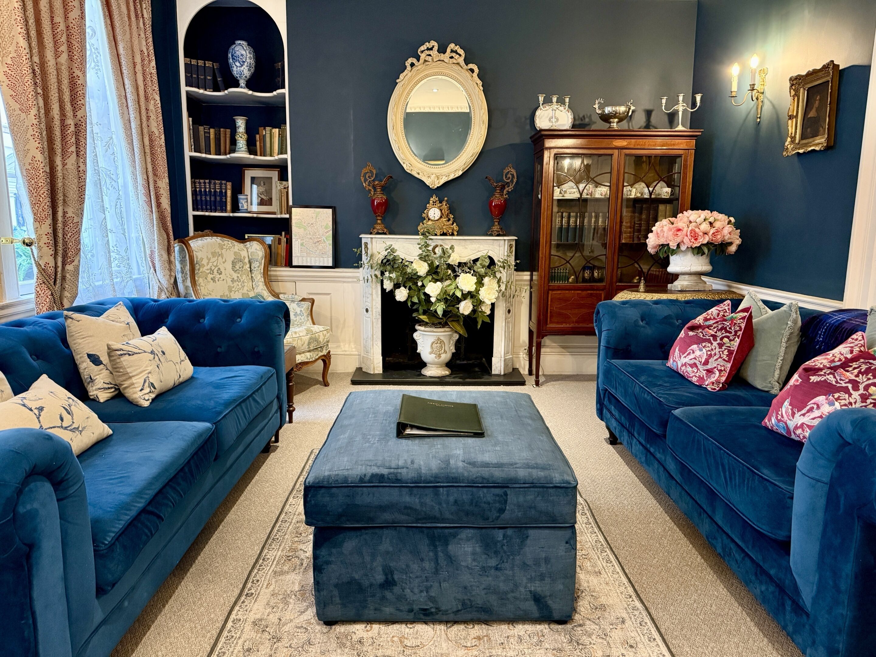 Ein Wohnzimmer mit zwei blauen Sofas, einem Kamin, einem Spiegel und einem Bücherregal.