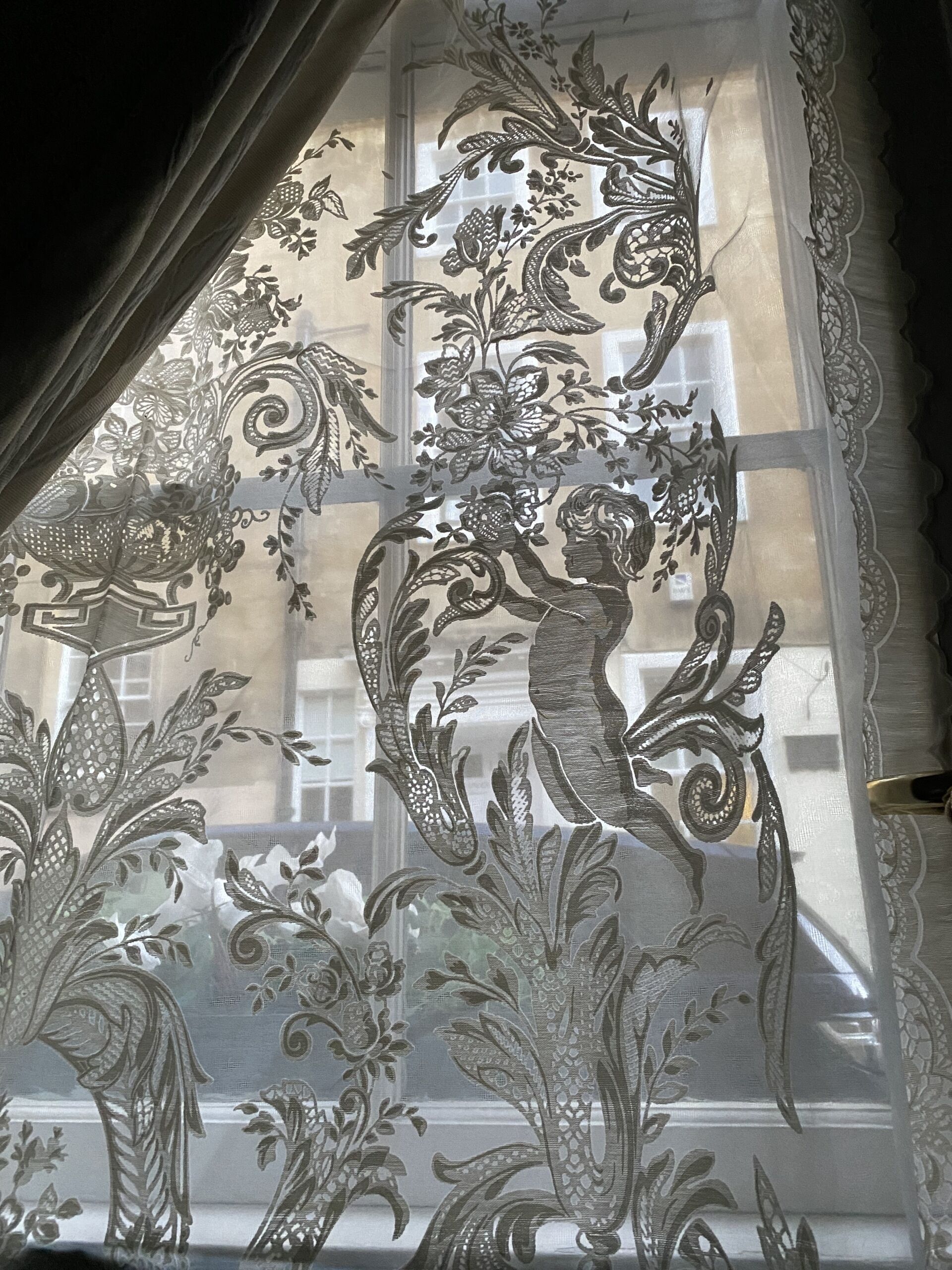 A window with intricate floral and faunal patterns, including a central figure of a woman and a bird.
