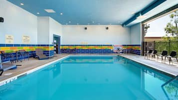 An indoor swimming pool with a tiled wall, lounge chairs, and safety signs.