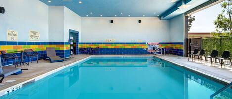 Piscina interna com parede revestida de azulejos, cadeiras de lounge e placas de segurança.