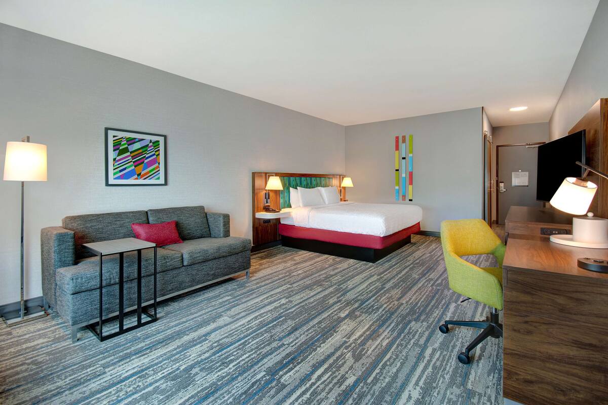 A hotel room with a bed, a sofa, a desk, and a chair.