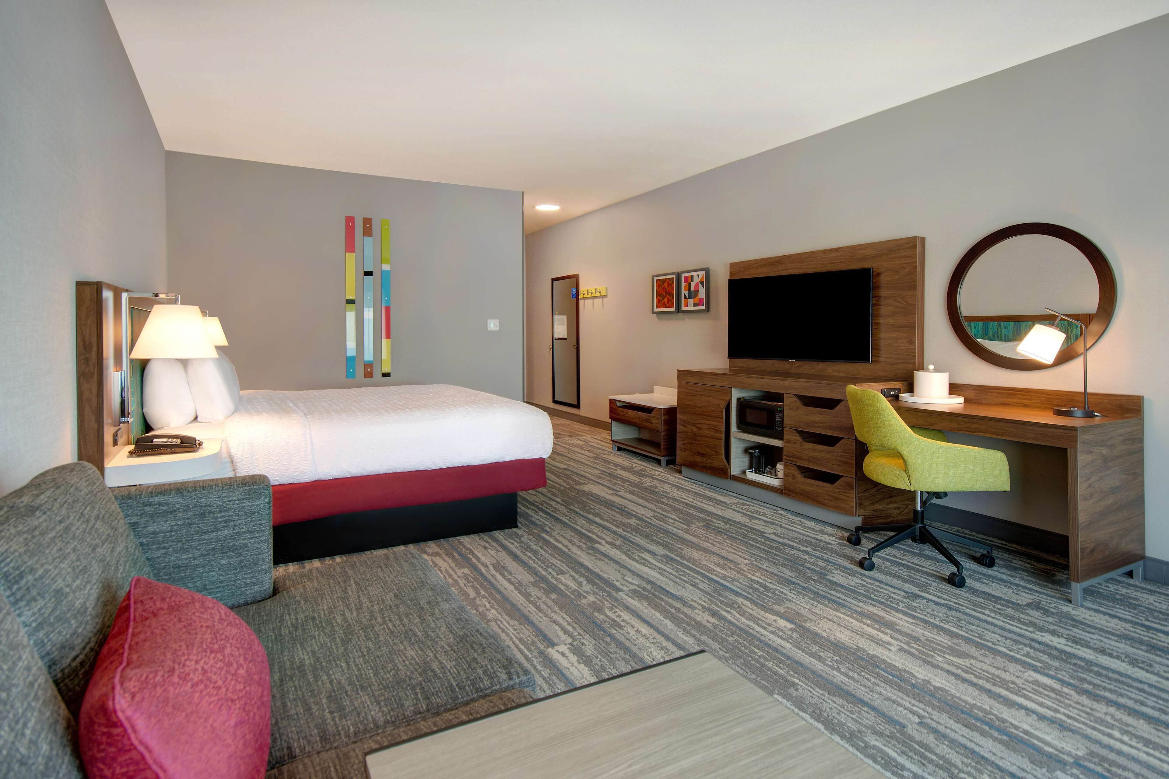 Une chambre d’hôtel avec un lit, un bureau, une chaise, une télévision et un miroir.
