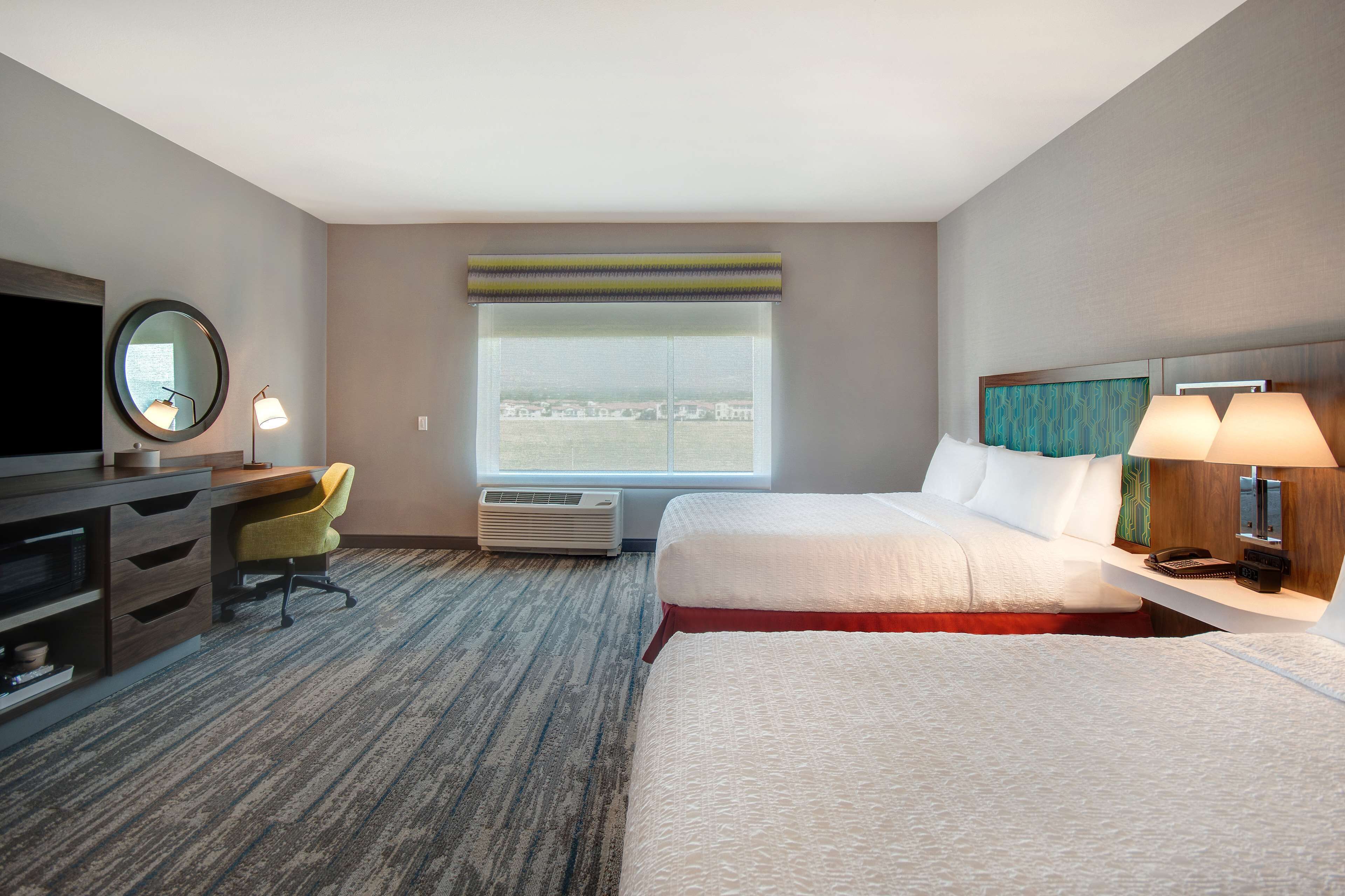 Habitación de hotel con dos camas, un escritorio con silla, televisor y ventana con vistas.