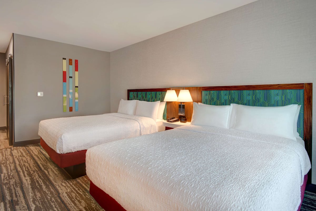 A hotel room with two beds, a wooden headboard, a wall-mounted lamp, and a patterned carpet.