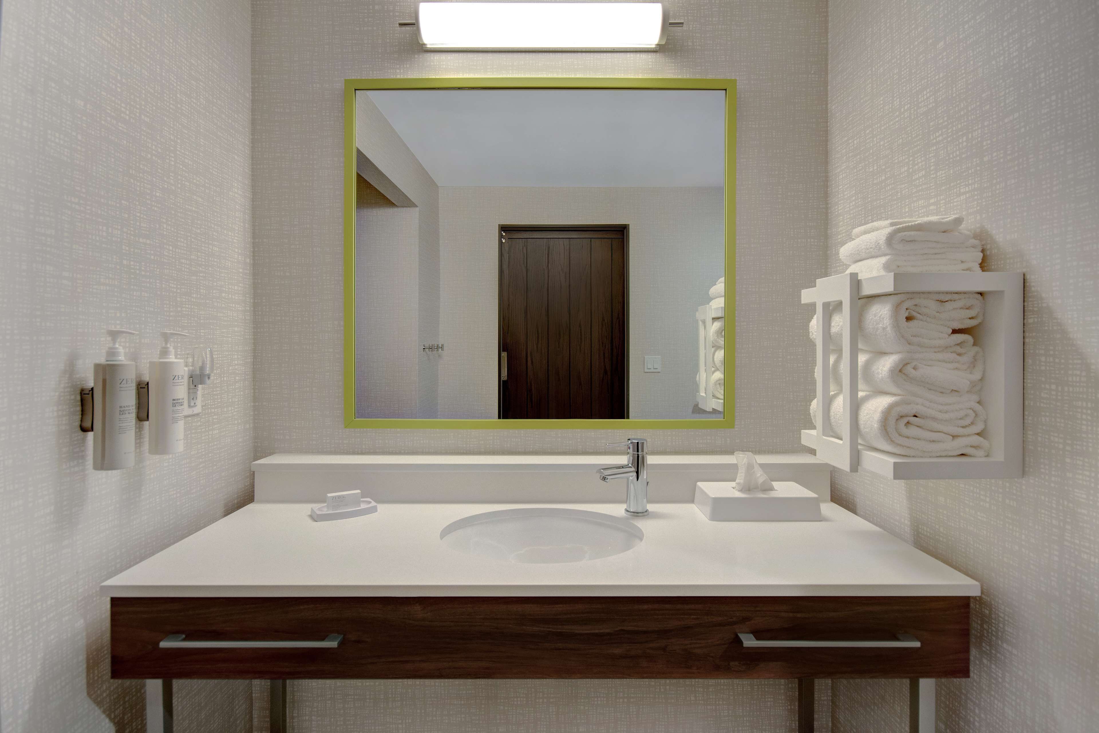 Un baño moderno con un lavamanos blanco, un espejo con marco verde y un perchero.