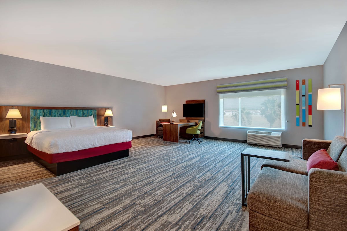 A hotel room with a bed, desk, chair, and a view of the outdoors.