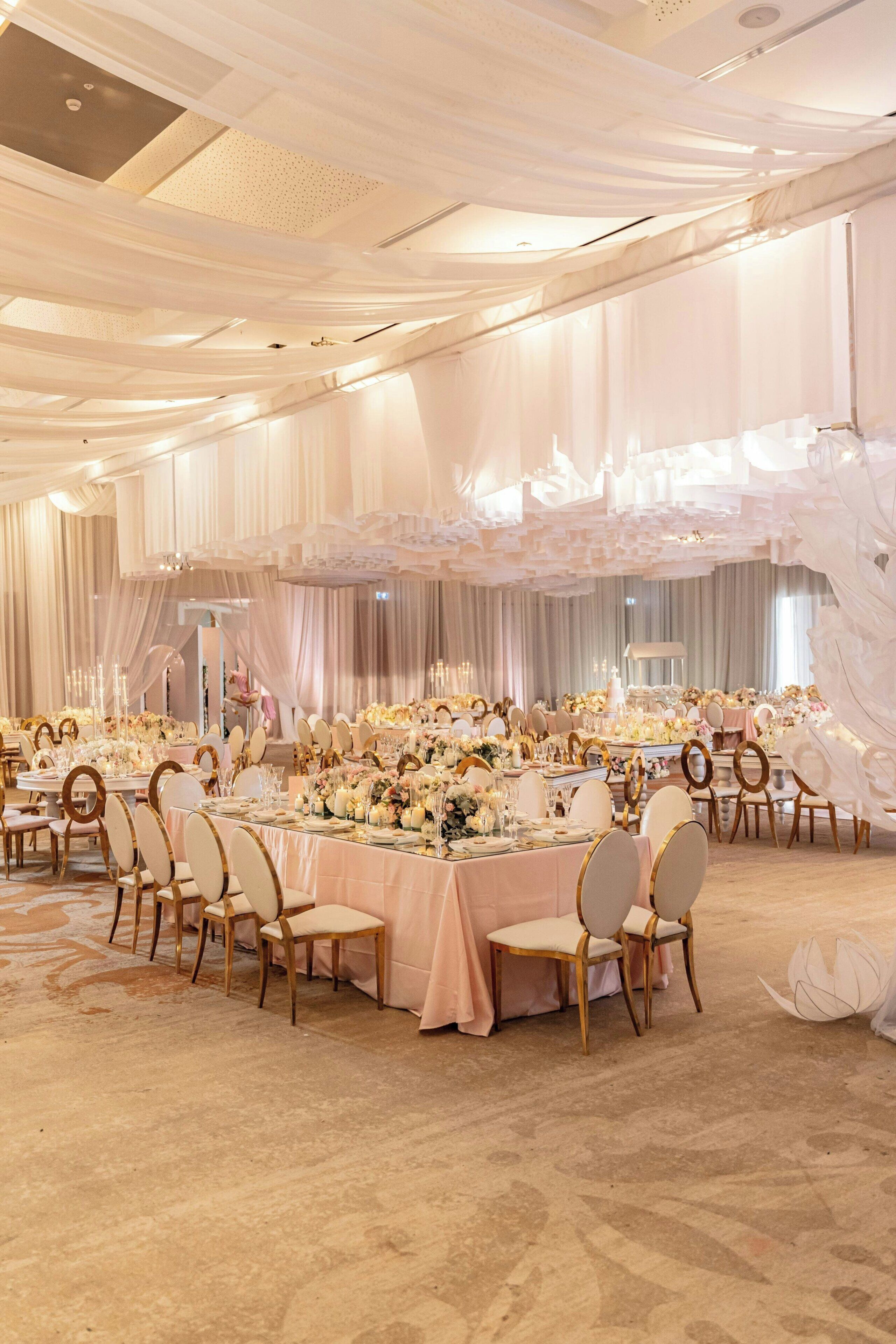 A banquet hall with round tables, chairs, and floral centerpieces.