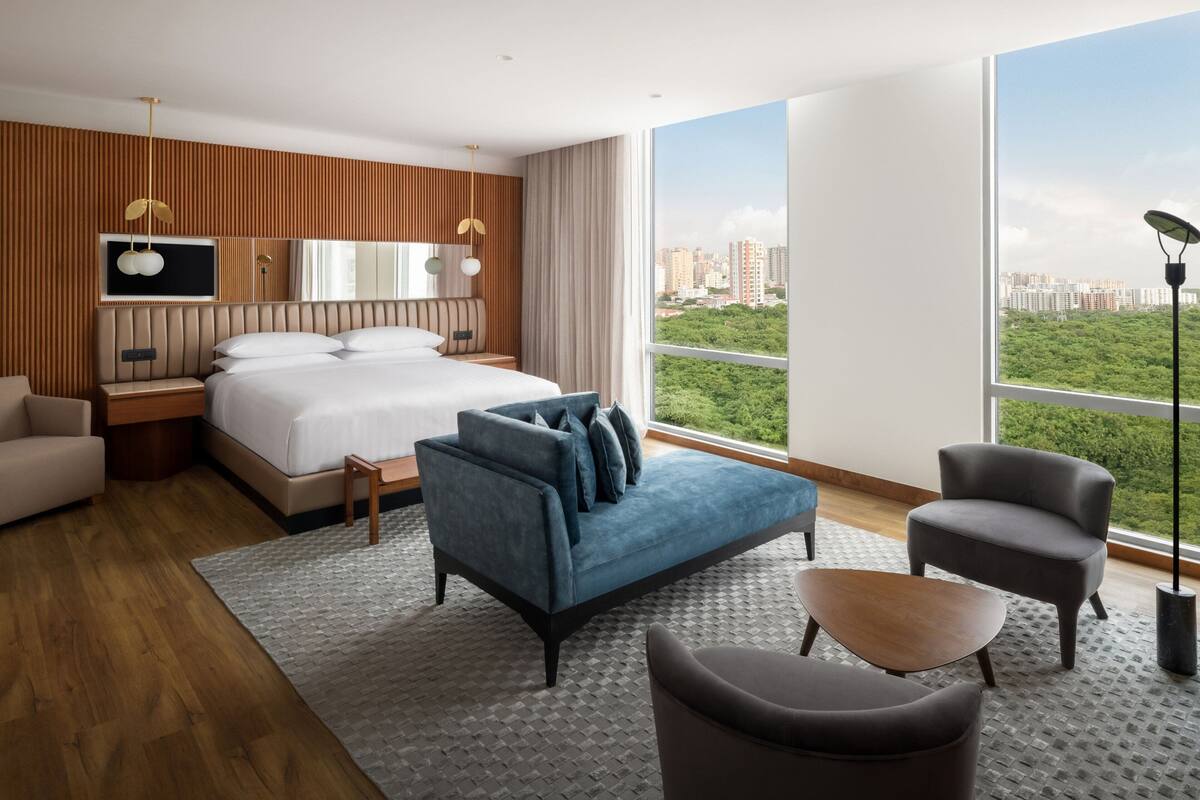 Une chambre d’hôtel moderne avec un grand lit, un canapé, un fauteuil et une vue sur la ville.