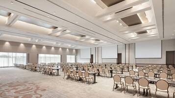 Un amplio salón de conferencias con filas de mesas y sillas, suelo alfombrado y techo alto con iluminación empotrada.