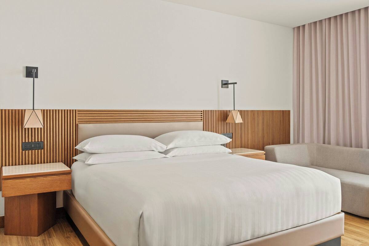 Une chambre d’hôtel moderne avec un grand lit, une tête de lit en bois, des tables de chevet et un canapé.