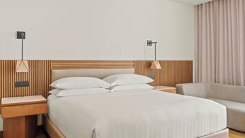 A modern hotel room with a large bed, wooden headboard, bedside tables, and a sofa.