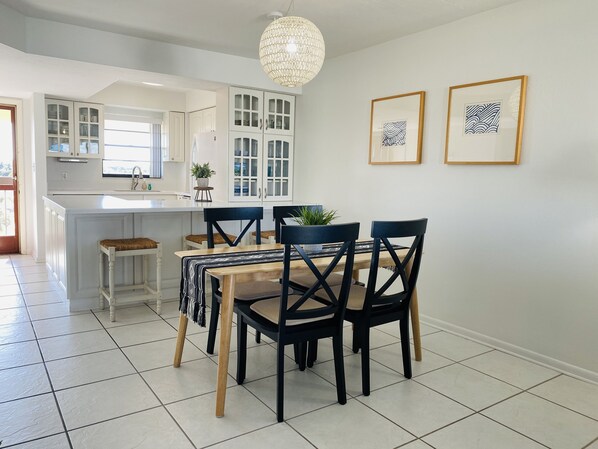 A modern kitchen with white cabinetry, a central island, and a dining area with a wooden table and black chairs. - Beautiful & spacious two bedroom waterfront condo (Marco Island)