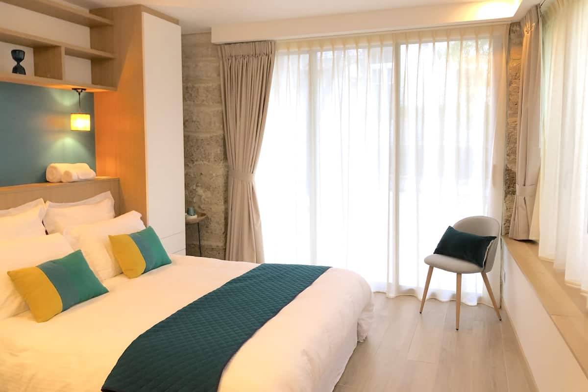 Ein Hotelzimmer mit einem großen Bett, einem Sessel am Fenster und einer Wand mit Steinverkleidung.