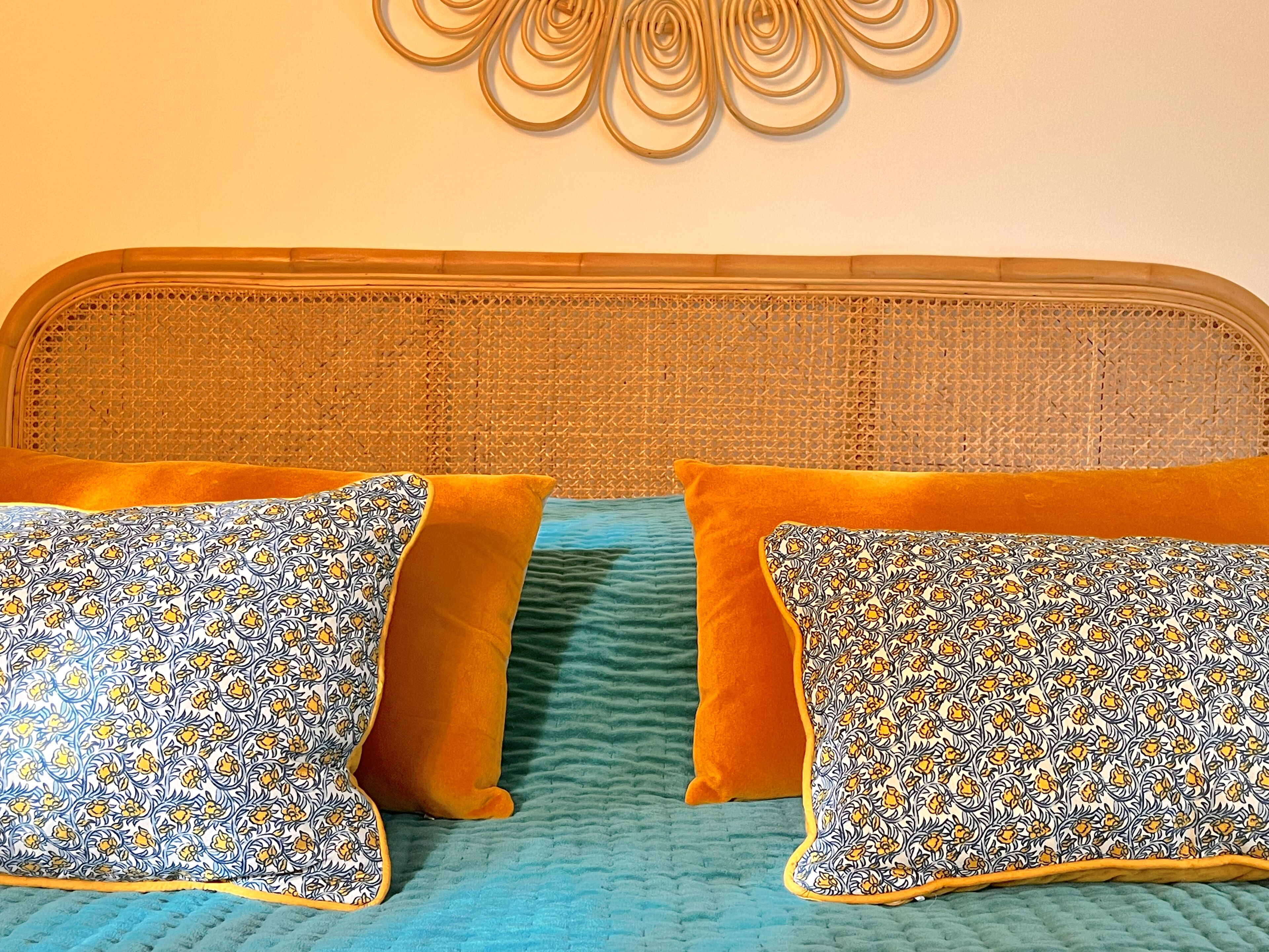 A bed with a woven headboard, two patterned pillows, and a teal bedspread.