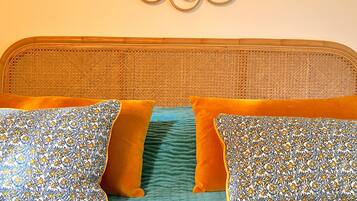 A bed with a woven headboard, two patterned pillows, and a teal bedspread.