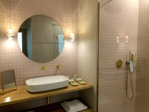 A bathroom with a large oval mirror, a white sink, a wooden vanity, a glass-enclosed shower, and a towel rack. - Les Nuits Pétillantes (Cournonterral)