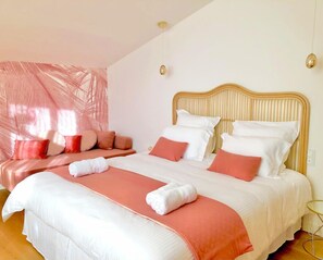 A hotel room with a large bed, a seating area with cushions, and a large window with a view of palm trees. - Les Nuits Pétillantes (Cournonterral)