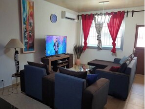 A living room with a flat-screen TV, sofas, a coffee table, and a lamp. - APPART LES LILLAS (Douala)