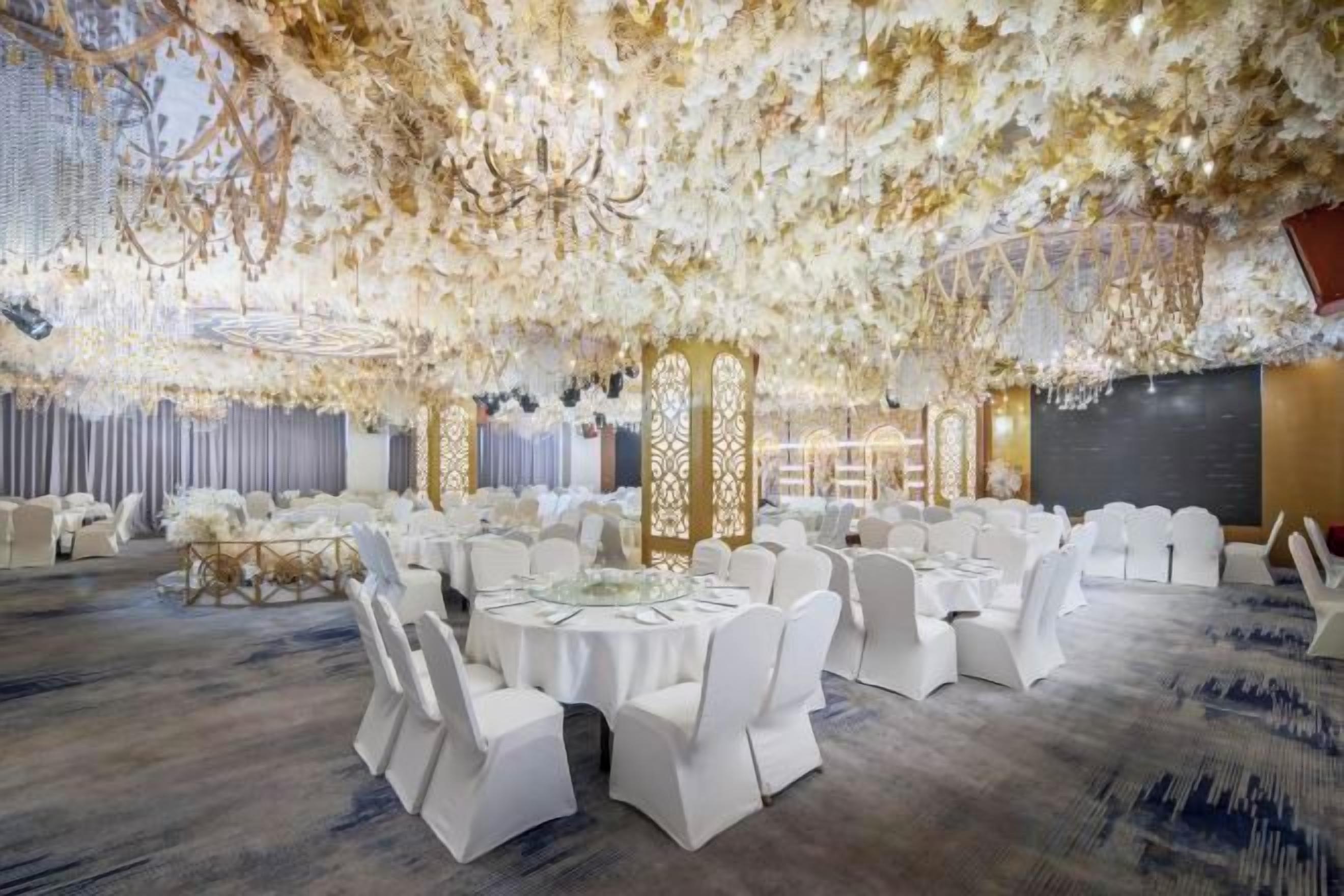 A banquet hall with round tables, white chairs, and a ceiling adorned with floral decorations.