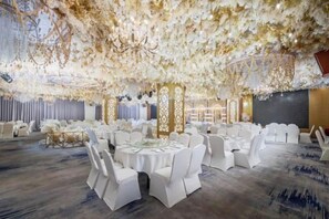 A banquet hall with round tables, white chairs, and a ceiling adorned with floral decorations.