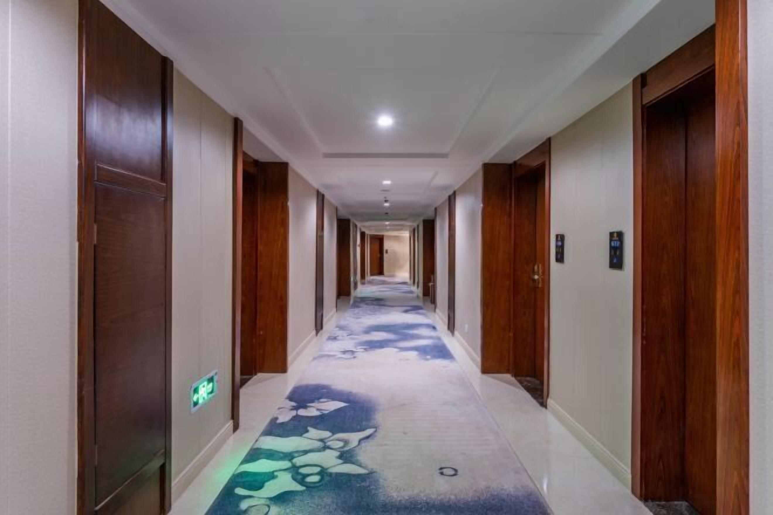 A hotel hallway with wooden doors, a patterned carpet, and a ceiling with recessed lighting.