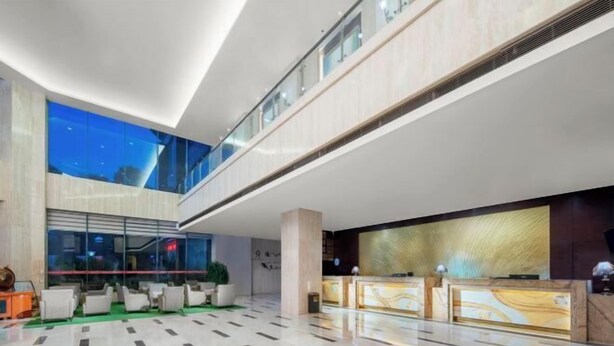 Un moderno vestíbulo de hotel con techo alto, una recepción, zona de estar y vistas al cielo nocturno a través de amplias ventanas.